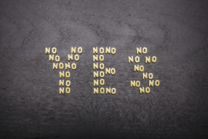 The answer "yes" made up of a set of words "no", with small pasta letters on a dark background of a wooden board, showing the hidden meaning and ambiguity of the agreement.